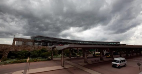 A modern airport building under a dramatic sky filled with dark, looming clouds.