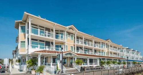 A coastal hotel with multiple balconies, surrounded by palm trees and a clear blue sky.