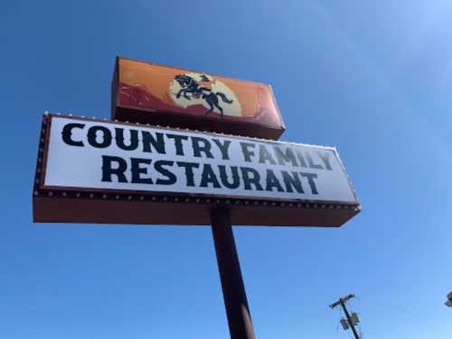 Sign for "Country Family Restaurant" featuring a cowboy on a horse against a blue sky.