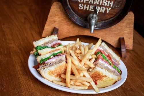 A plate with a layered sandwich filled with greens and meats, served with a side of golden French fries.