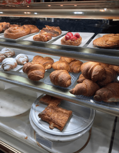 A display case filled with various pastries, including croissants, danishes, and a fruit tart.