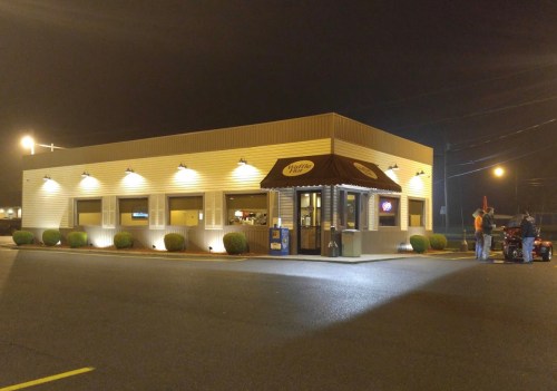 A well-lit fast-food restaurant at night, featuring a drive-thru and a couple of people outside.