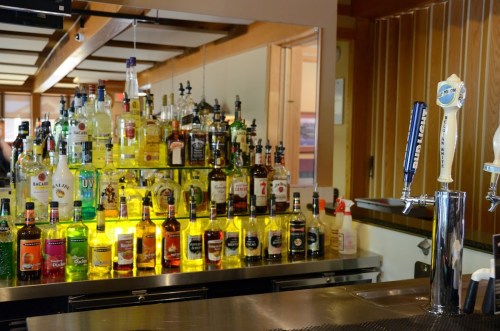 A well-stocked bar featuring various bottles of liquor and a beer tap, with a warm wooden interior.