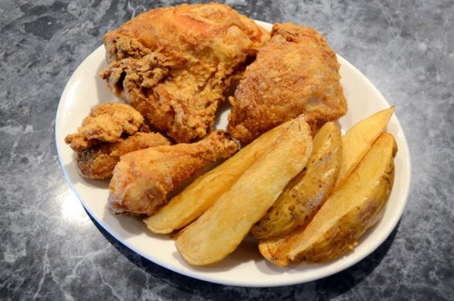 A plate of crispy fried chicken pieces alongside golden-brown potato wedges on a gray marble surface.