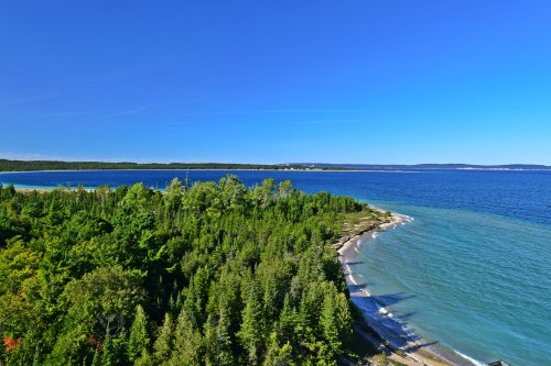 A scenic view of a coastline with lush green trees meeting a calm blue lake under a clear blue sky.