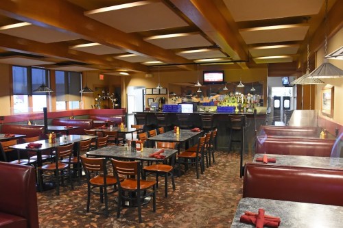 Interior of a restaurant featuring booths, tables, and a bar area with a TV and decorative lighting.