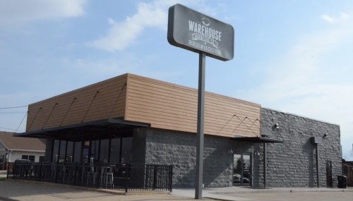 Exterior of a modern brewery with a wooden roof and large windows, featuring a sign that reads "Warehouse Beerhouse."