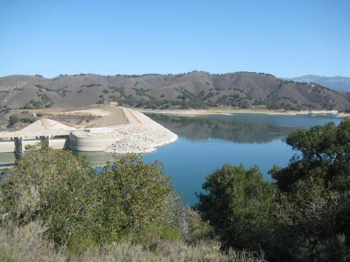 A serene landscape featuring a calm reservoir surrounded by hills and greenery under a clear blue sky.