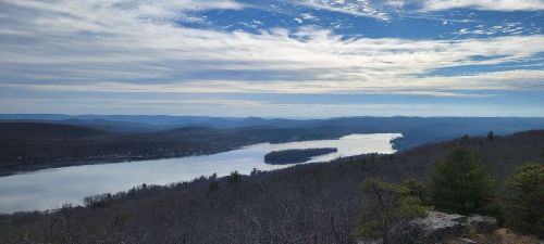 A panoramic view of a serene lake surrounded by hills under a cloudy sky.
