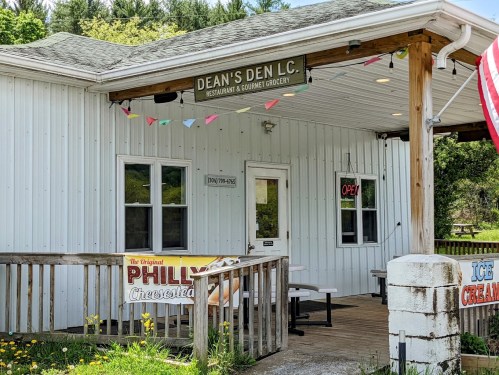 Exterior of Dean's Den L.C., a restaurant and grocery, featuring a porch with seating and an "Open" sign.