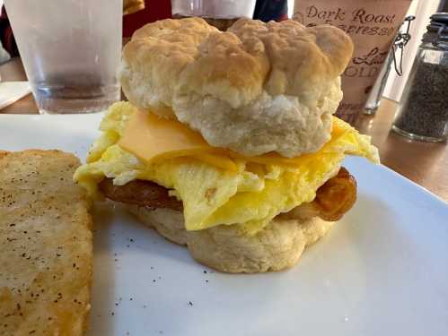 A fluffy biscuit sandwich with cheese, scrambled eggs, and sausage, served with a side of hash browns.