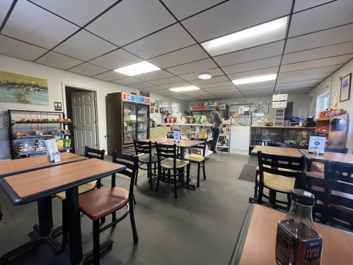 A cozy café interior with tables, a counter displaying snacks, and a person browsing the shelves.