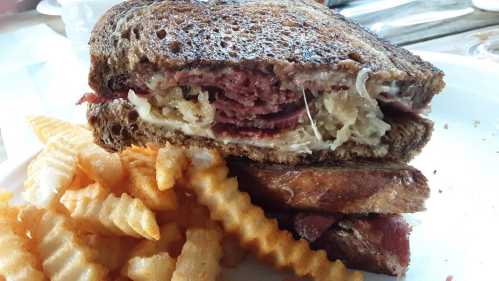 A close-up of a toasted sandwich filled with meat and sauerkraut, served with crinkle-cut fries on the side.