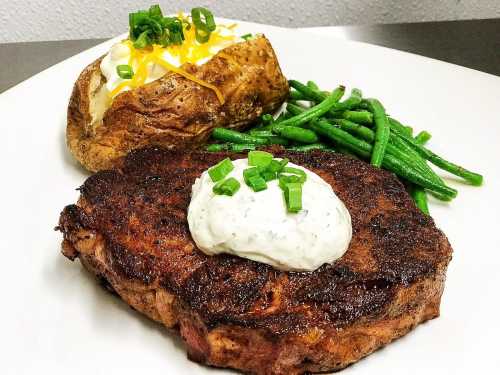 A plate featuring a grilled steak topped with sour cream and green onions, alongside a baked potato and green beans.