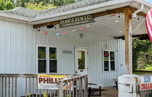 A white building with a sign reading "Dean's Den L.C." and an open sign, featuring a porch and colorful decorations.