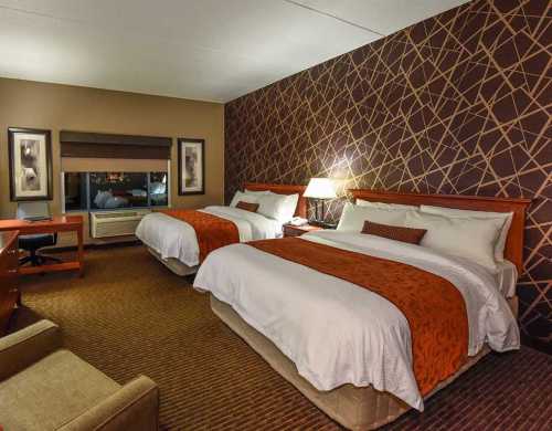 Cozy hotel room with two beds, a desk, and warm decor featuring a patterned accent wall.