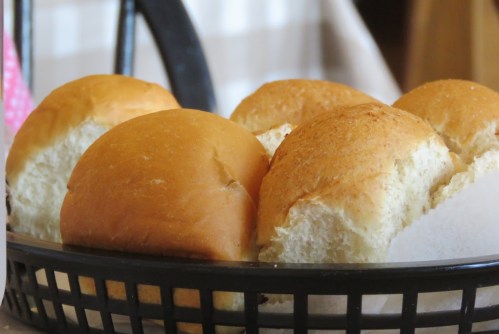 A basket of freshly baked dinner rolls, golden brown and soft, arranged neatly on a table.