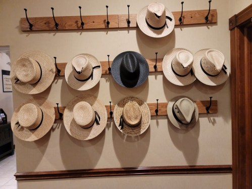 A wall display featuring various straw and felt hats hanging on hooks.