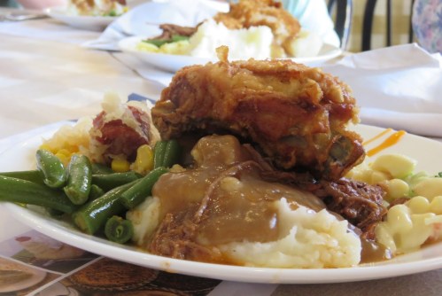 A plate of comfort food featuring fried chicken, mashed potatoes with gravy, green beans, and corn.