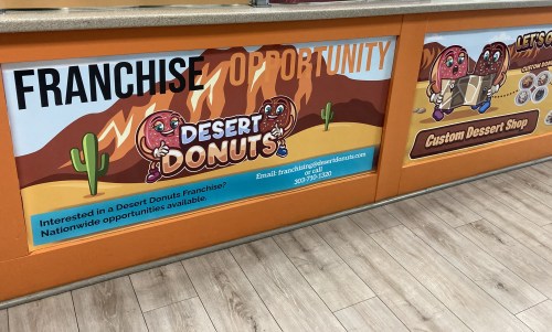 Banner promoting a franchise opportunity for Desert Donuts, featuring cartoon donuts and desert scenery.