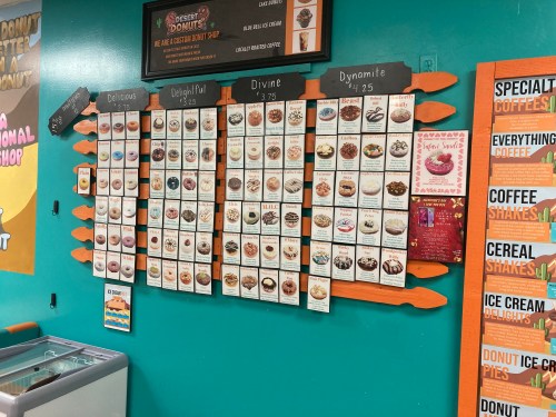 Menu board featuring various donut options with prices, displayed on a colorful wall in a donut shop.