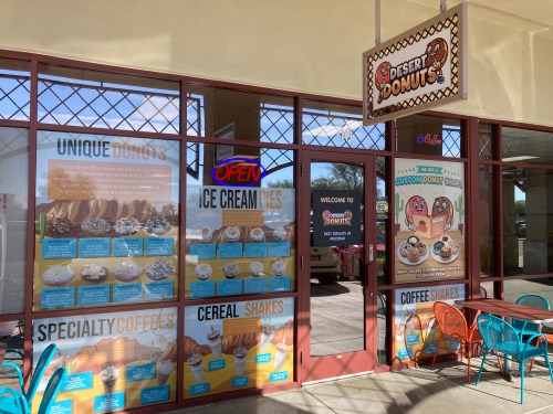 Exterior of Desert Donuts shop featuring colorful signage, menu boards for donuts, ice cream pies, and shakes.