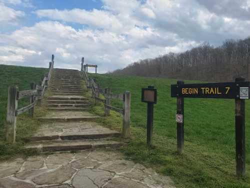 Stone steps lead up a grassy hill, with a sign marking the start of Trail 7 against a cloudy sky.