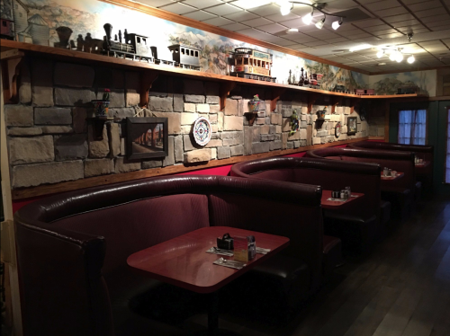 Cozy restaurant interior with curved booths, red tables, and decorative stone walls featuring vintage items.