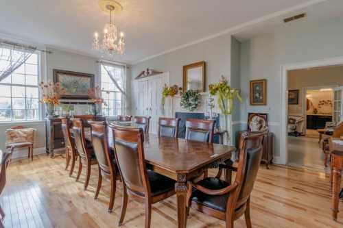 A spacious dining room with a large wooden table, elegant chairs, and a chandelier, featuring light-colored walls and decor.