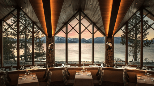 Elegant restaurant interior with large windows showcasing a scenic lake and mountains at sunset.