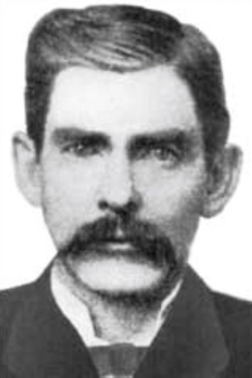 Black and white portrait of a man with a mustache, wearing a suit and tie, looking directly at the camera.