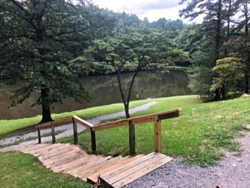 A wooden staircase leads down to a calm lake surrounded by trees and greenery.