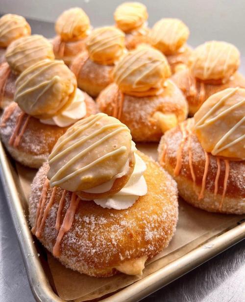 A tray of fluffy donuts topped with cream, orange drizzle, and cookie-like decorations.
