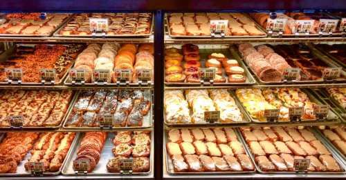 A display case filled with various baked goods, including cookies, pastries, and donuts, all labeled with prices.
