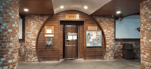 A rustic entrance with a wooden door, brick walls, and a sign reading "4041" above it. Notices are posted nearby.