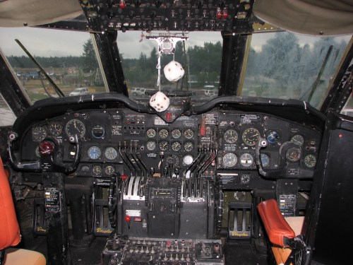 Cockpit of an aircraft featuring various gauges, controls, and levers, with a view of the windshield and dashboard.