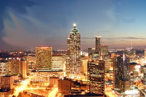 A vibrant city skyline at dusk, featuring tall buildings and illuminated streets in a bustling urban landscape.