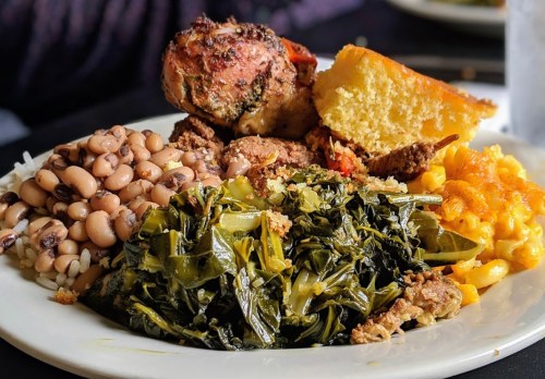 A plate of Southern comfort food featuring black-eyed peas, collard greens, fried chicken, cornbread, and macaroni and cheese.