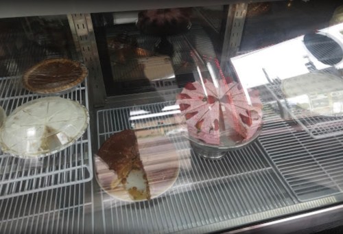 A display case with various desserts, including a slice of pie and a whole cake, all under glass.