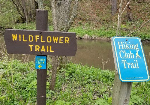 A wooden sign for "Wildflower Trail" next to a blue sign for "Hiking Club Trail" near a creek in a wooded area.