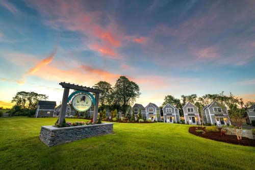 A scenic view of East Island Reserve with a sign, surrounded by green grass and houses under a colorful sunset sky.