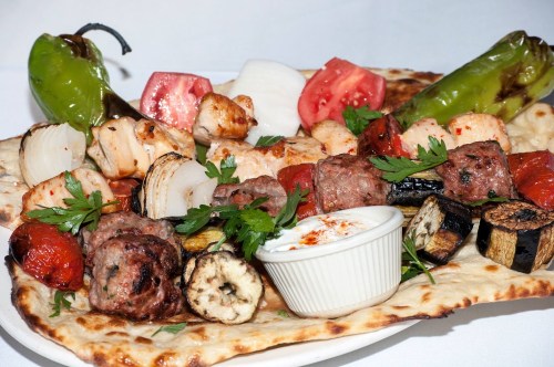 A colorful platter featuring grilled meats, vegetables, and a side of yogurt sauce on a bed of flatbread.