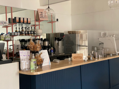 A cozy café counter with coffee machines, pastries, and a menu displayed on a wooden surface.
