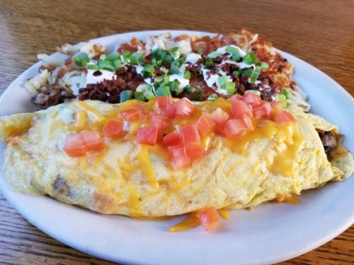 A plate featuring a cheese and tomato omelet alongside crispy hash browns topped with green onions and sour cream.