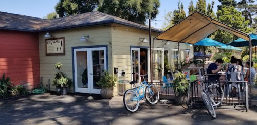 A colorful café with outdoor seating, bicycles parked outside, and patrons enjoying their time on a sunny day.