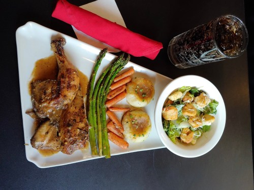 A plate with roasted chicken, mashed potatoes, asparagus, carrots, and a side salad, accompanied by a drink.