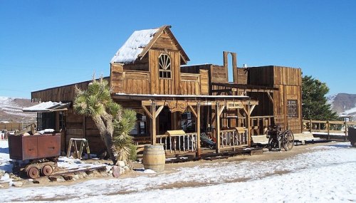 A rustic wooden building in a snowy landscape, resembling an old Western town with a clear blue sky.
