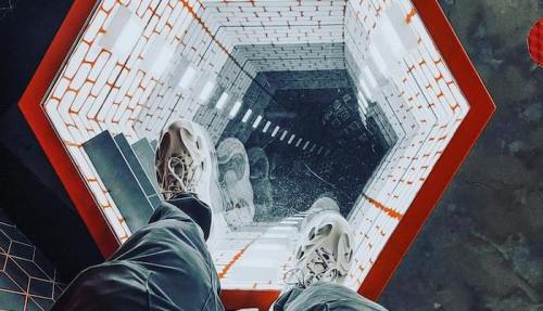 A person stands above a hexagonal mirror installation, creating a dizzying illusion of depth below.