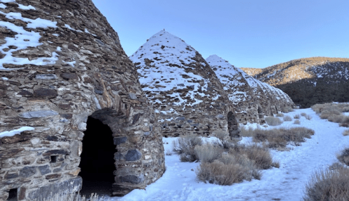 Stone kilns with snowy roofs, set against a mountainous landscape and a clear blue sky.