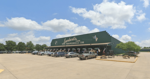 A large green building with "Lambert's Cafe" signage, surrounded by trees and parked vehicles under a cloudy sky.